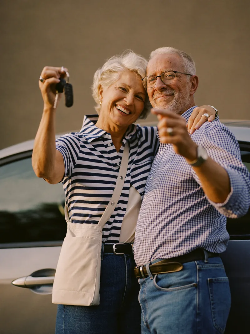 A happy older couple standing by their new car, holding up the keys.